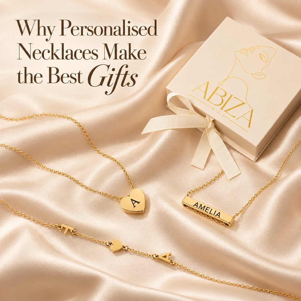 Why Personalised Necklaces Make the Best Gifts — a gold initial heart locket, an engraved Amelia bar necklace and a letter station necklace on cream silk beside an Abiza gift box