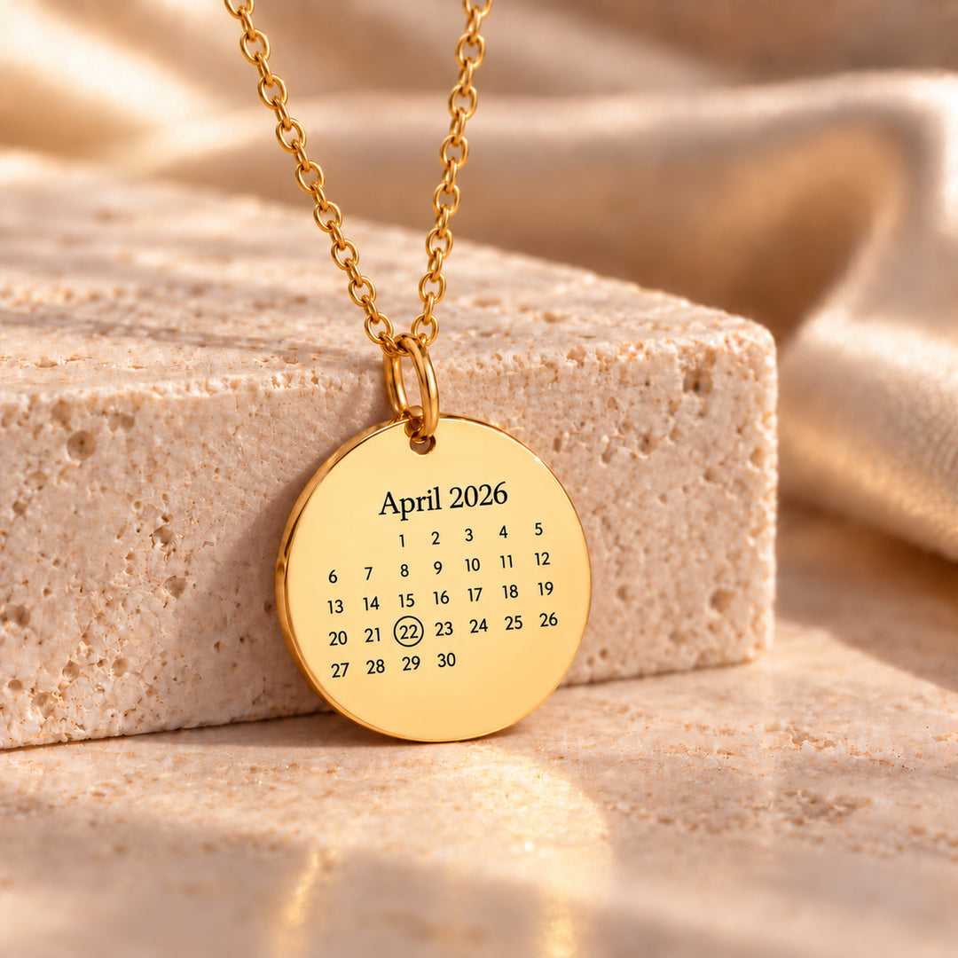 Gold calendar necklace with an engraved month and one date circled on a polished 21mm disc