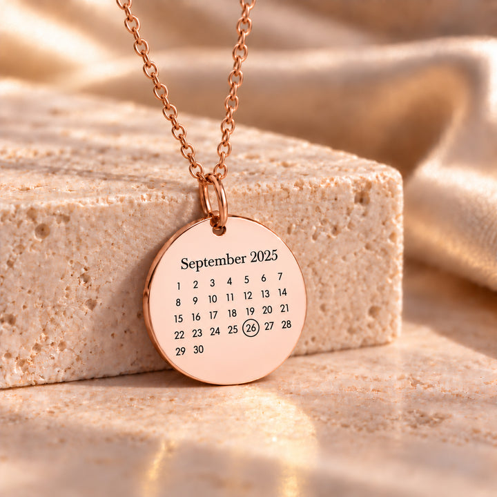 Rose gold calendar necklace with an engraved month and circled date
