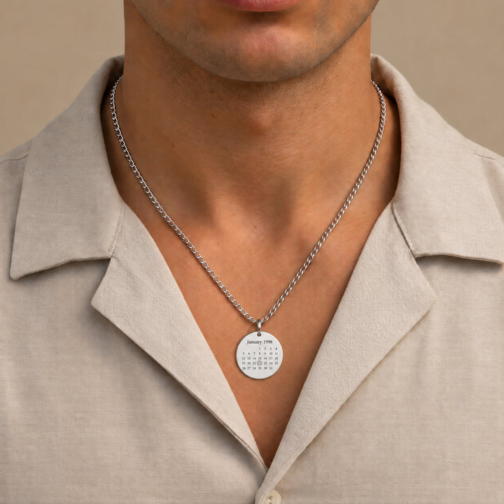 Silver calendar necklace engraved with January 1998, worn by a man on a Cuban chain