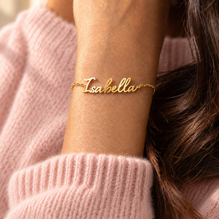 Gold script name bracelet worn on the wrist, name cut in flowing script