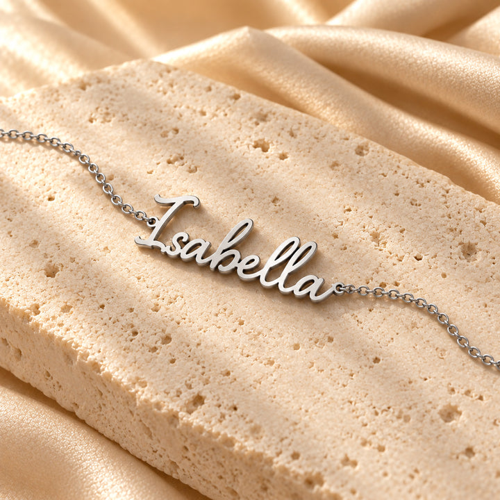 Silver script name bracelet on a dainty chain, flat lay on stone