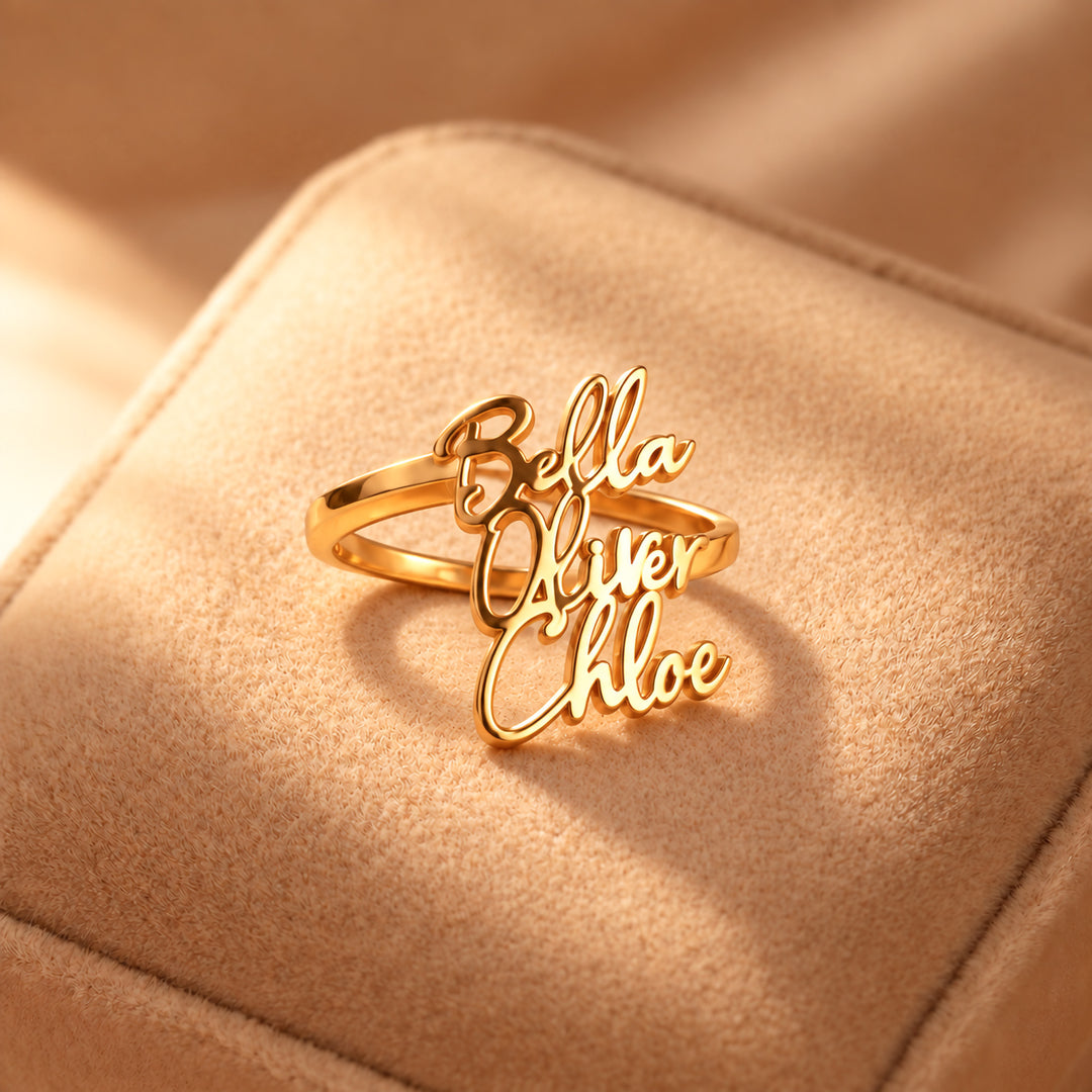 Gold personalised name ring with three names, Bella, Oliver and Chloe, on a suede cushion