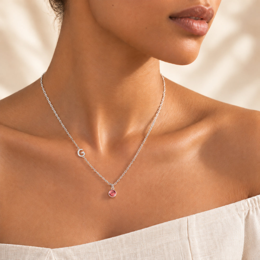 Model wearing a silver sideways initial necklace with letter G and a pink October birthstone charm