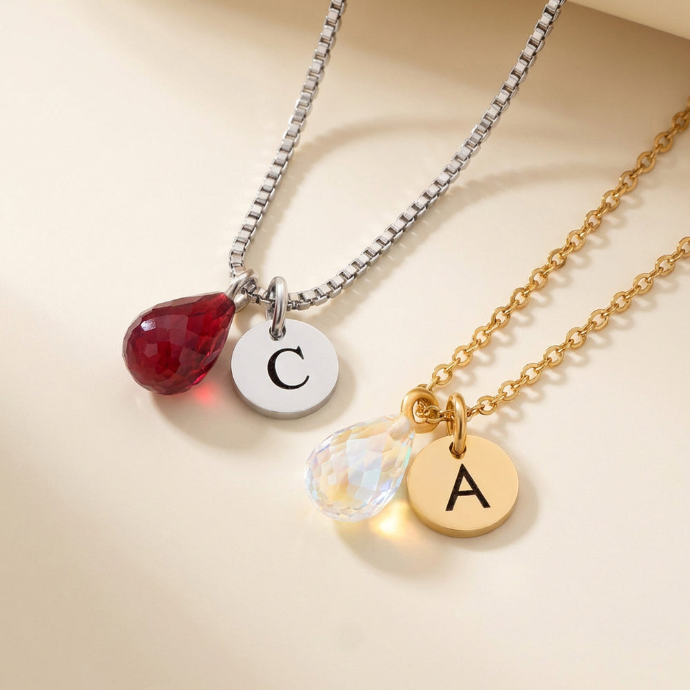 Birthstone necklace with initial disc — teardrop crystal birthstone alongside engraved letter charm