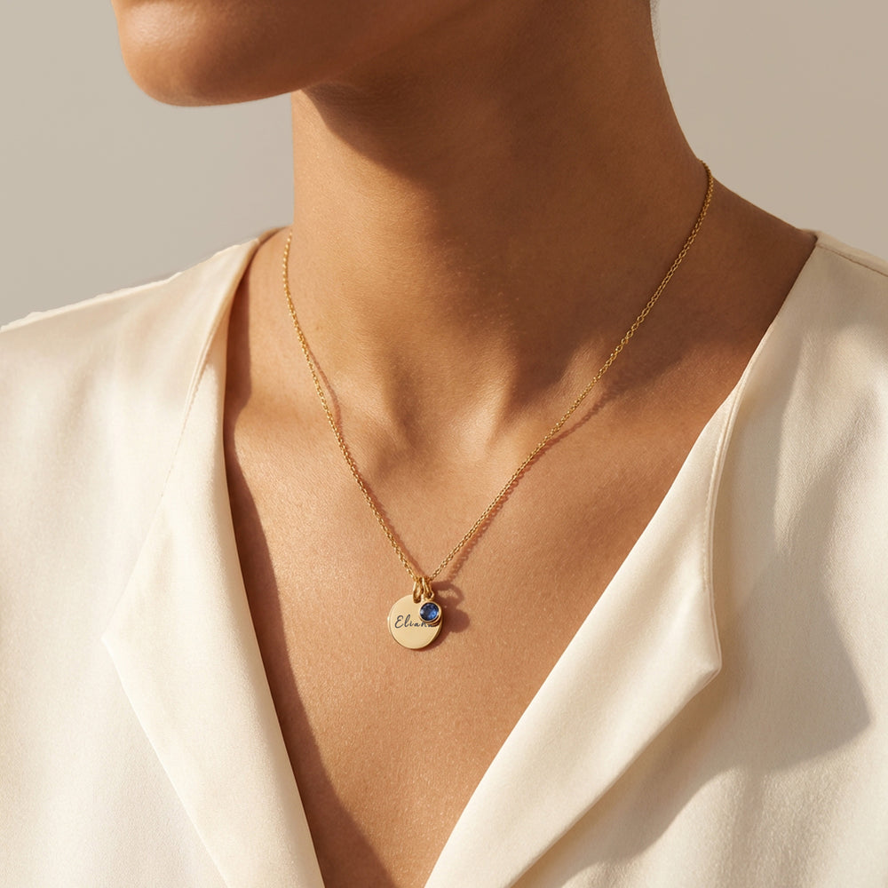 Model wearing birthstone name necklace in gold with engraved coin and September birthstone charm