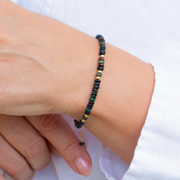 Real Black Opal Bracelet with black, green, and gold beads on a wrist wearing a white long-sleeve shirt — Abiza.