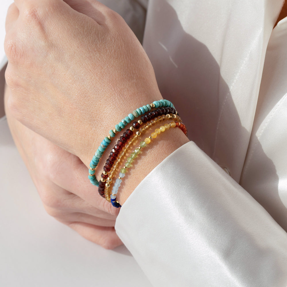 14K gold filled garnet bracelet on wrist stacked with other Abiza bracelets— real January birthstone with deep wine-red colour