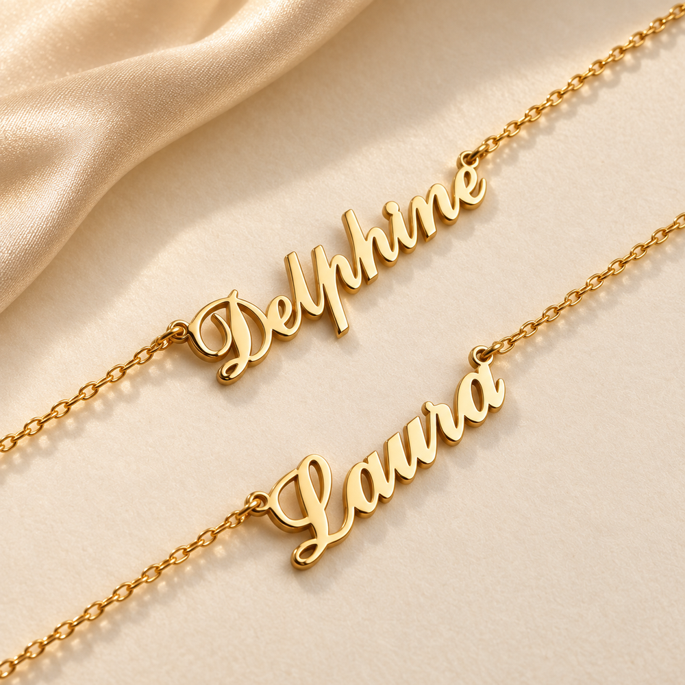 Two gold Carrie name necklaces with the names Delphine and Laura