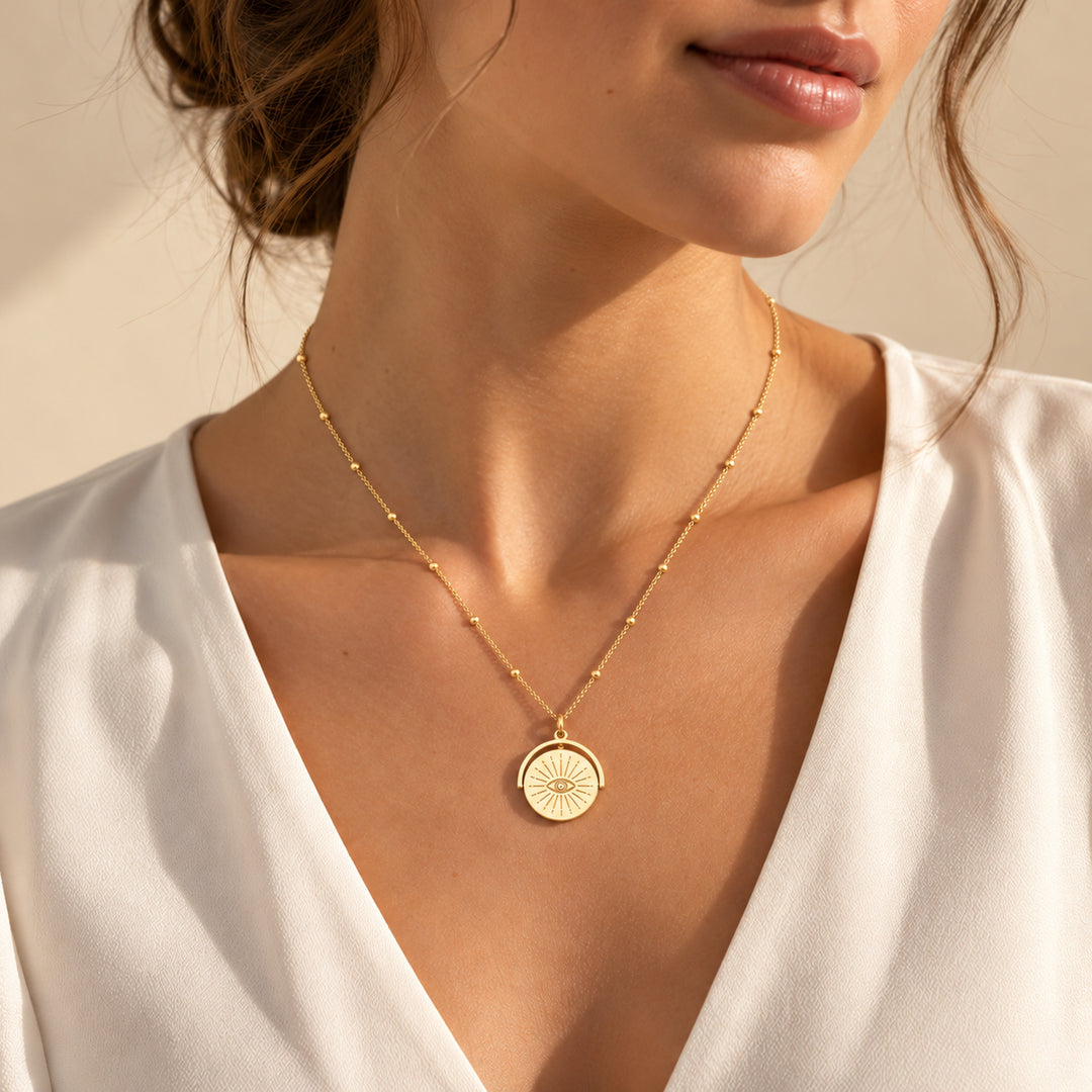 Model wearing a gold evil eye spinner necklace with a sunburst engraved disc