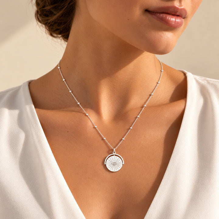Model wearing a silver evil eye spinner necklace on a beaded chain