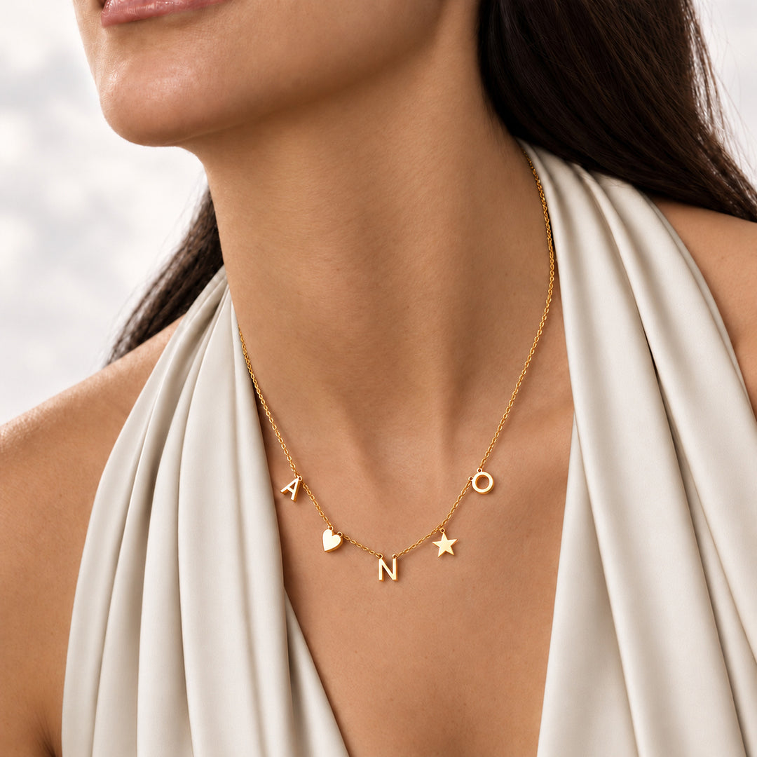 Gold dainty initial necklace worn with multiple letters and heart and star charms
