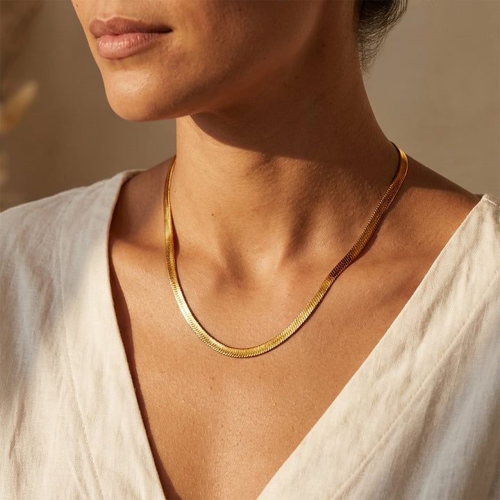 Woman wearing gold snake chain herringbone necklace in a sunny afternoon