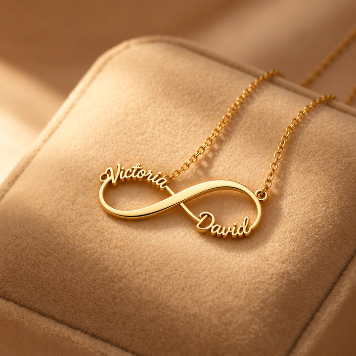Gold infinity name necklace with two names in script, on a suede cushion