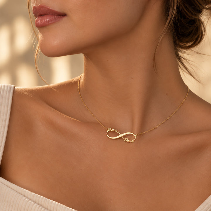 Gold infinity name necklace with two names in script, worn on the neck