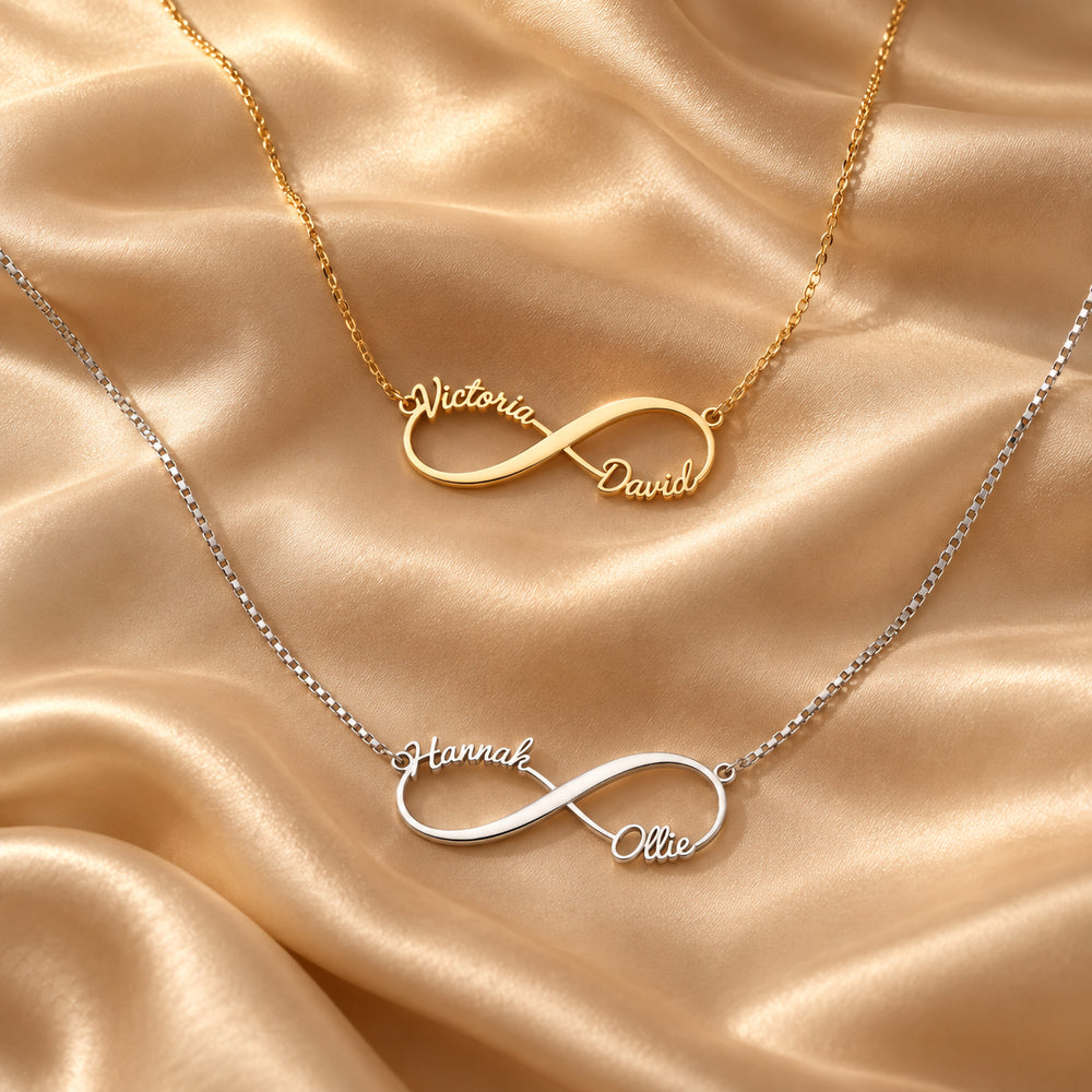 Gold and silver infinity name necklaces, each with two names in script, flat lay on satin