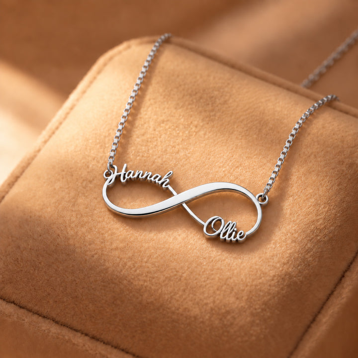 Silver infinity name necklace with two names in script on a box chain, on a suede cushion