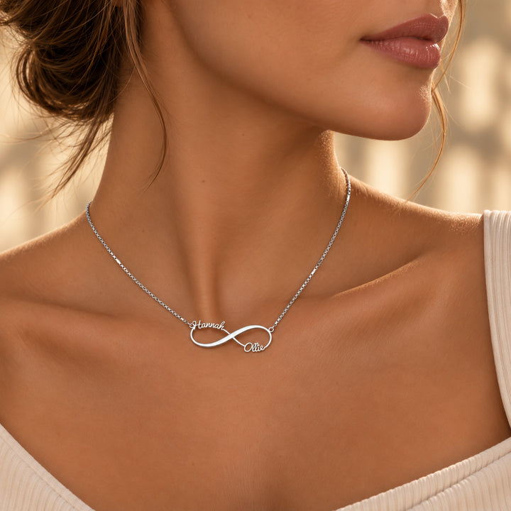 Silver infinity name necklace with two names in script on a box chain, worn on the neck