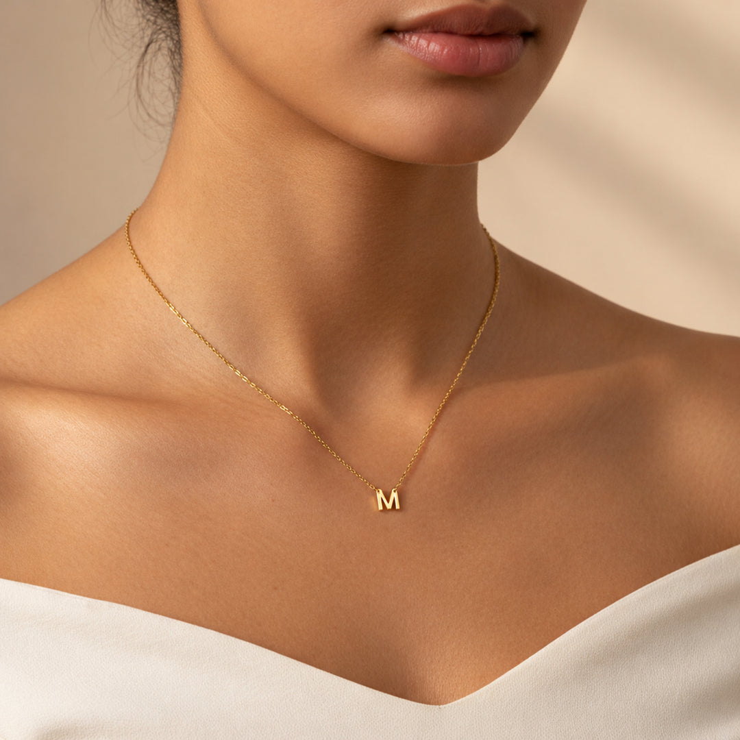 Model wearing a dainty 18K gold initial necklace with a hanging letter M pendant