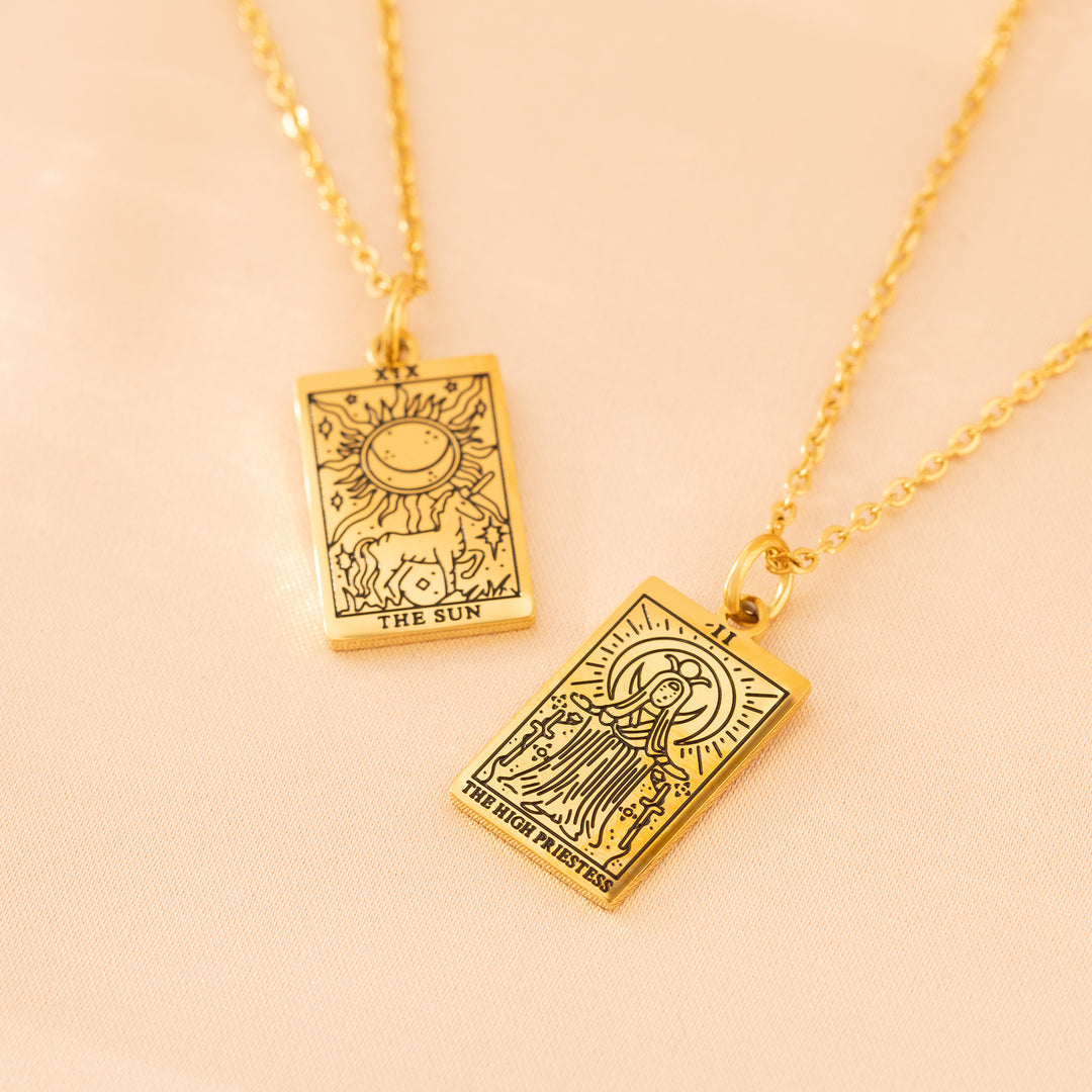Gold tarot card necklace pendants on light pink background