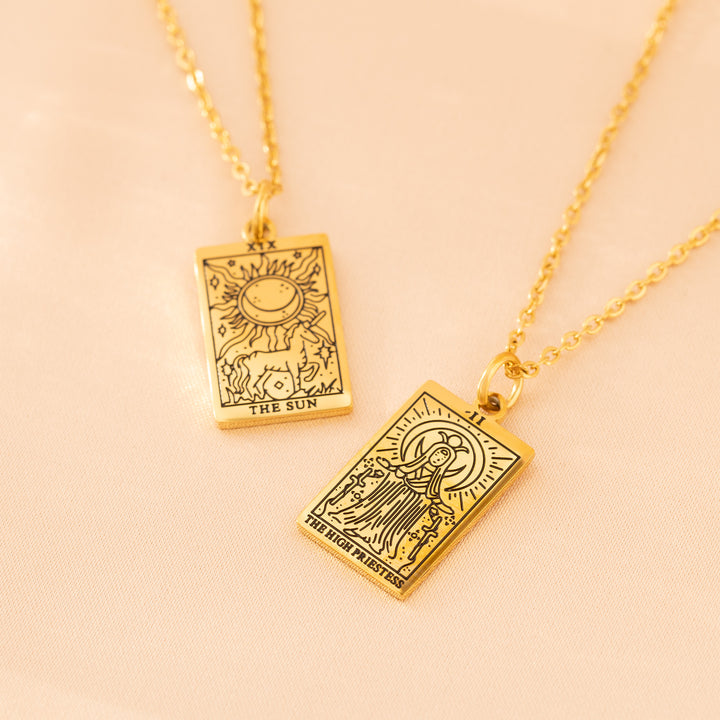 Gold tarot card necklace pendants on light pink background