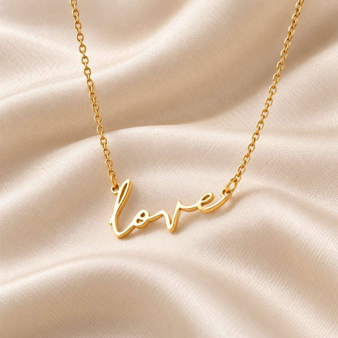 Gold love script necklace shown flat, love written in script