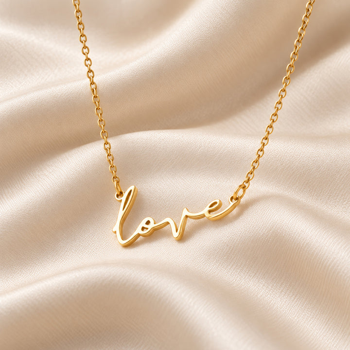 Gold love script necklace shown flat, love written in script