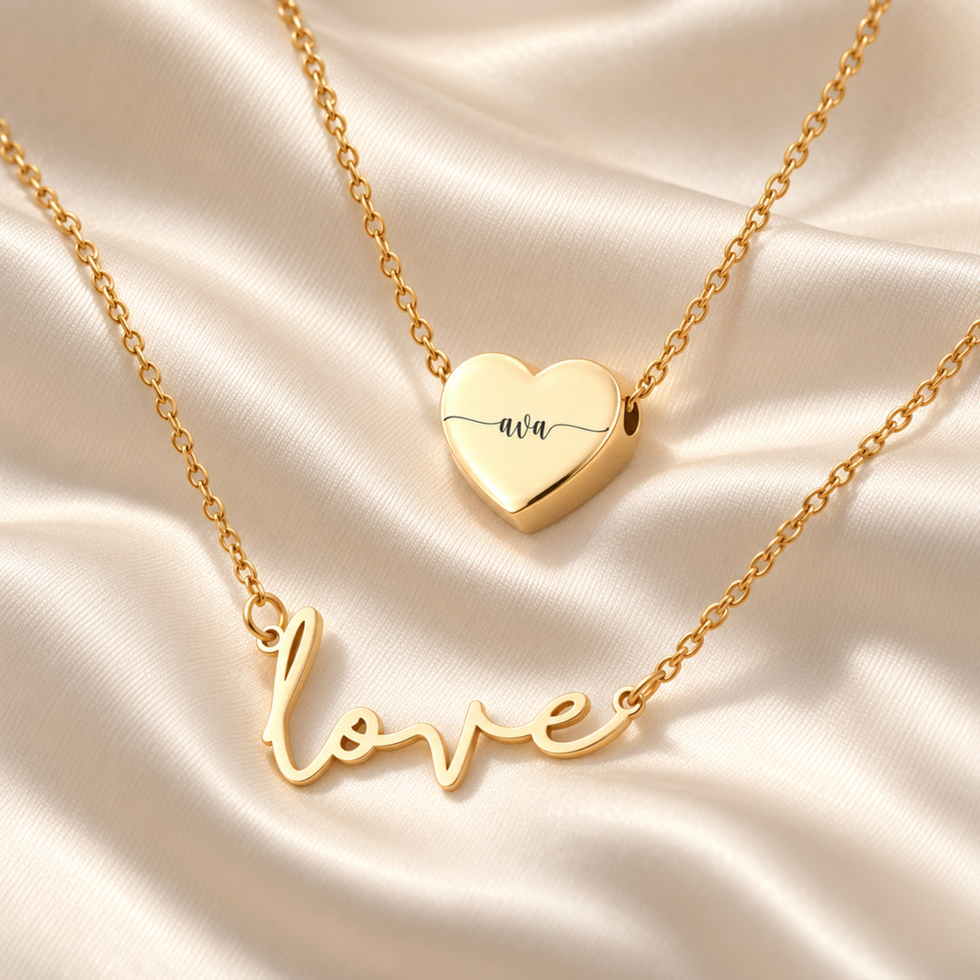 Gold love script necklace layered with an engraved heart name pendant
