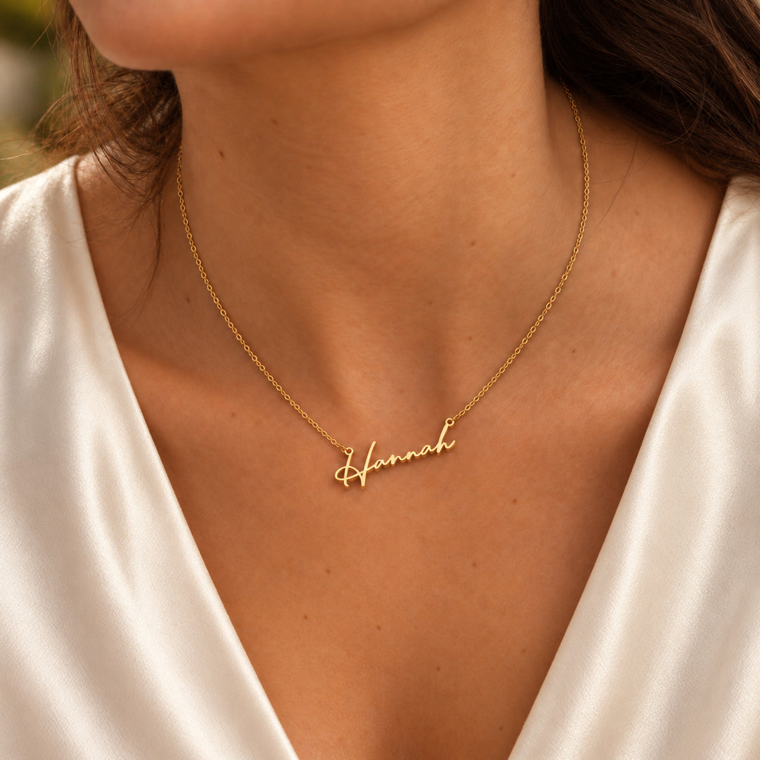Dainty gold name necklace in a fine script font, worn on model