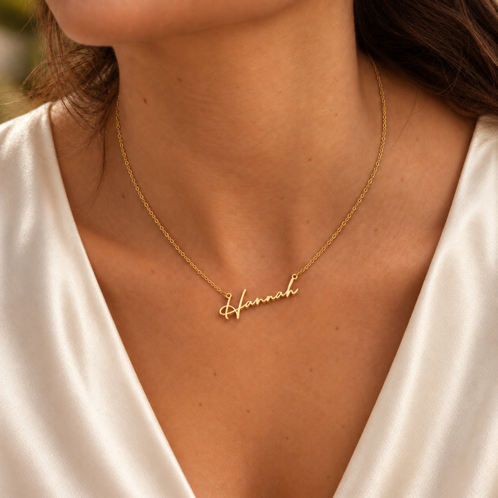 Dainty gold name necklace in a fine script font, worn on model
