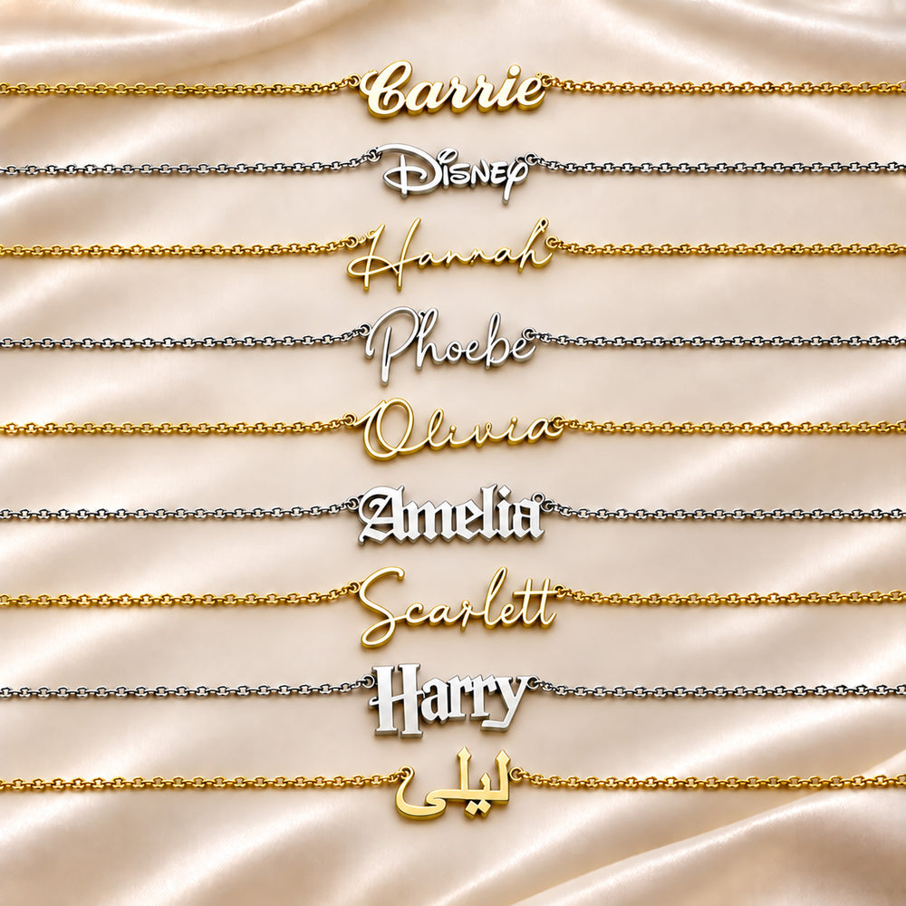 Nine personalised name necklaces are arranged horizontally on a draped champagne satin background. The necklaces feature custom script names including Carrie, Hannah, Phoebe, Olivia, Amelia, Scarlett, Harry shown in both gold and silver metal finishes.