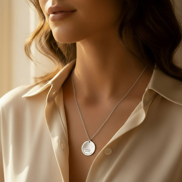 Close-up of a woman wearing a silver newborn necklace with a pendant.