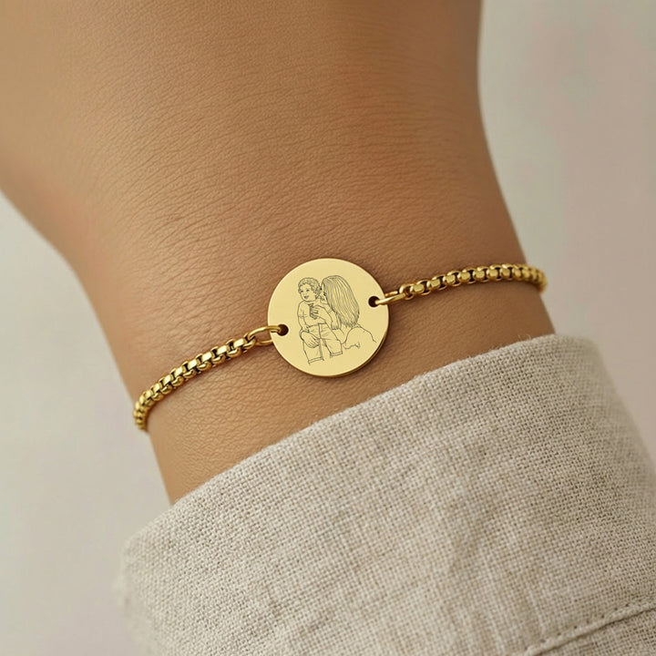 Gold bracelet with a circular photo engraved charm on a wrist against a neutral background