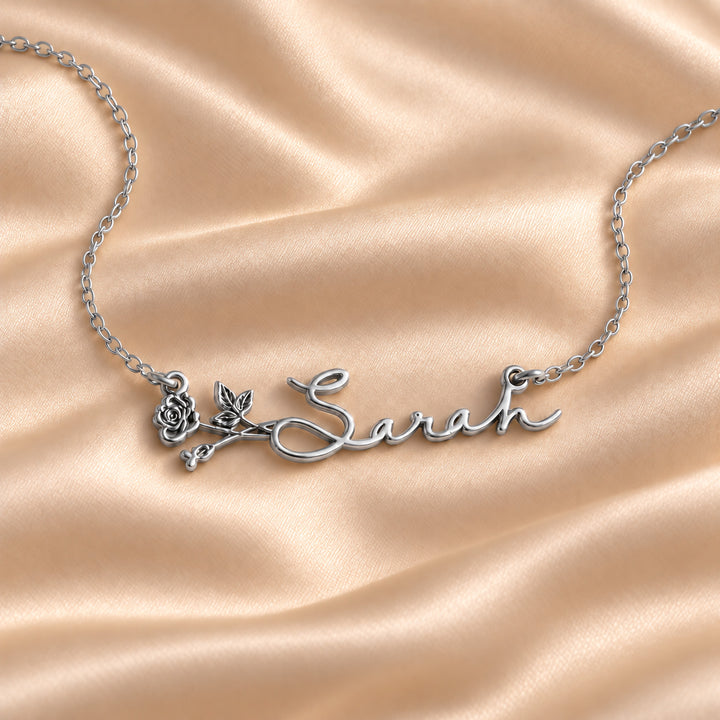 Silver birth flower name necklace with the name Sarah and a rose, flat lay on satin