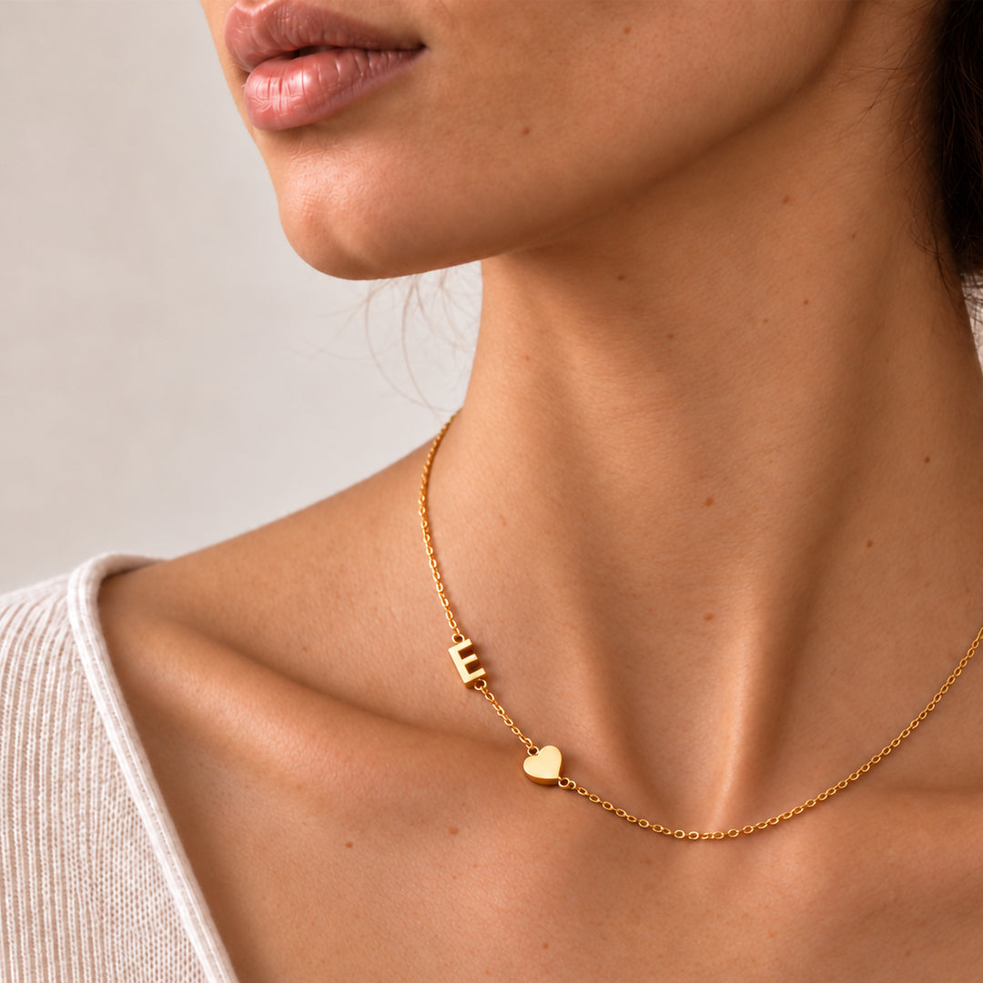 Woman wearing a gold sideways initial necklace with a single letter E beside a heart charm