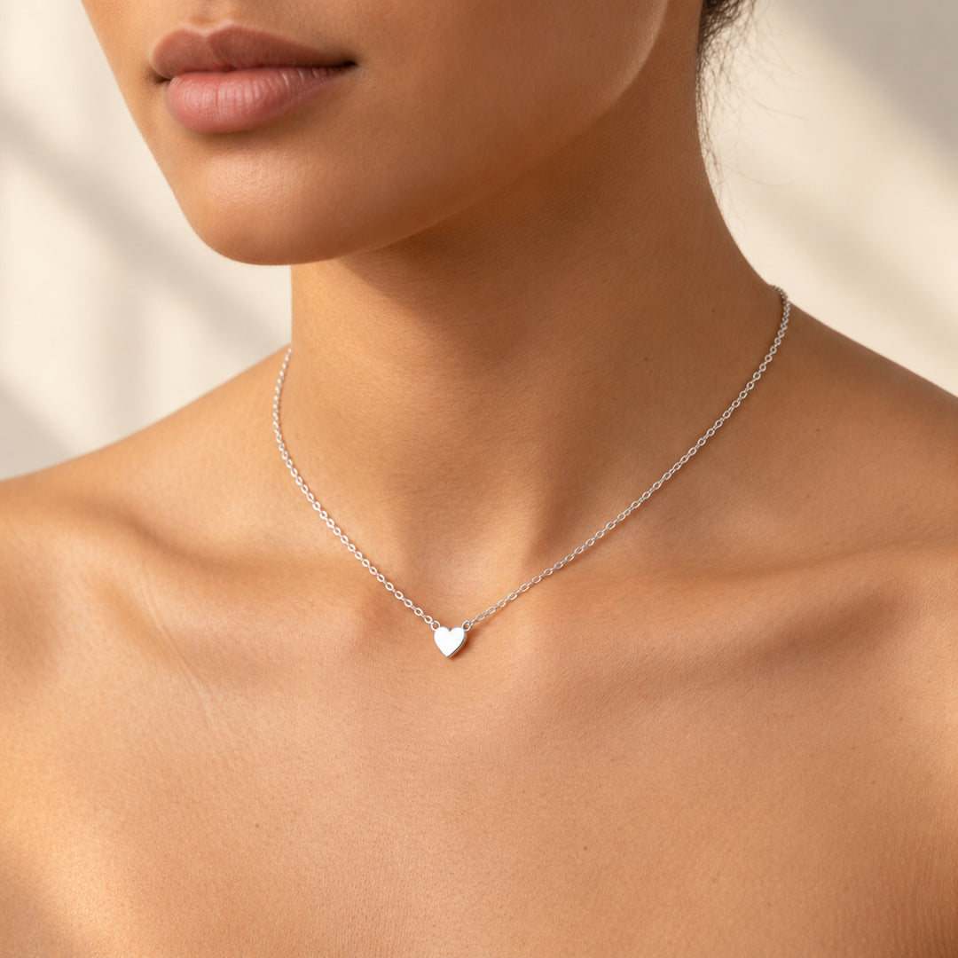 Model wearing a dainty silver necklace with a tiny heart charm