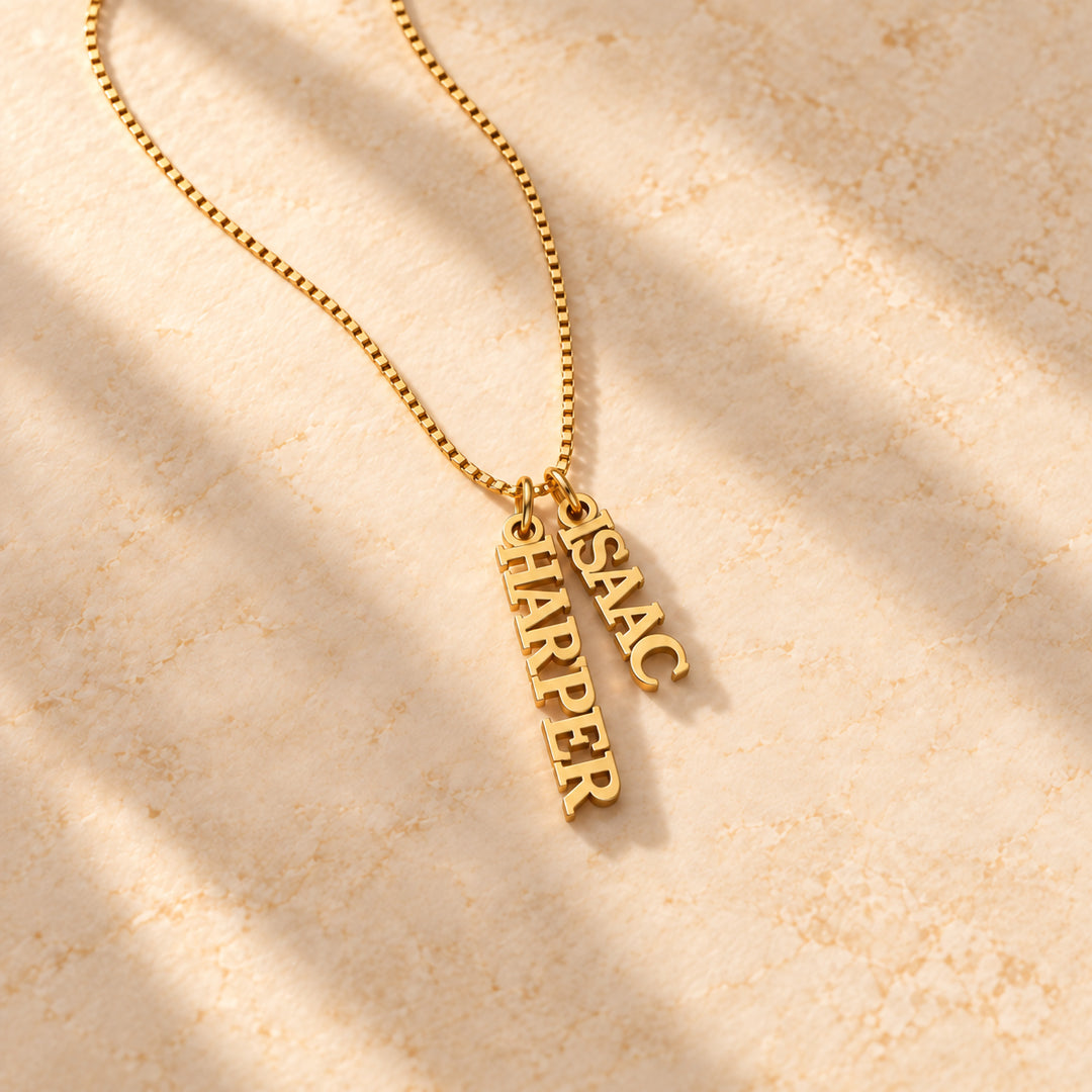 Gold vertical name plate necklace with two names in block capitals on a box chain, flat lay