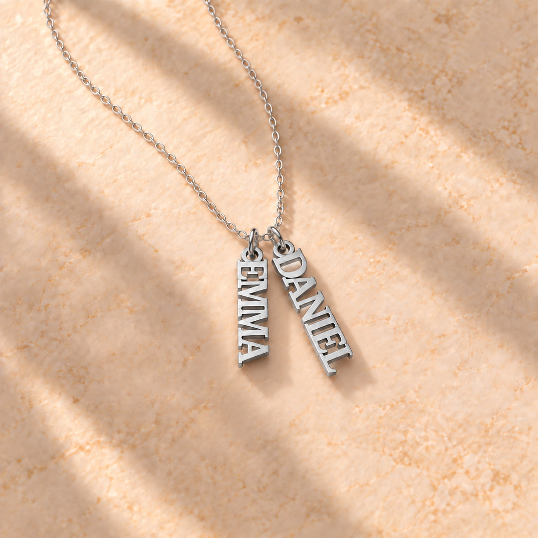 Silver vertical name plate necklace with two names in block capitals on a cable chain, flat lay