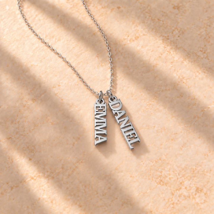 Silver vertical name plate necklace with two names in block capitals on a cable chain, flat lay