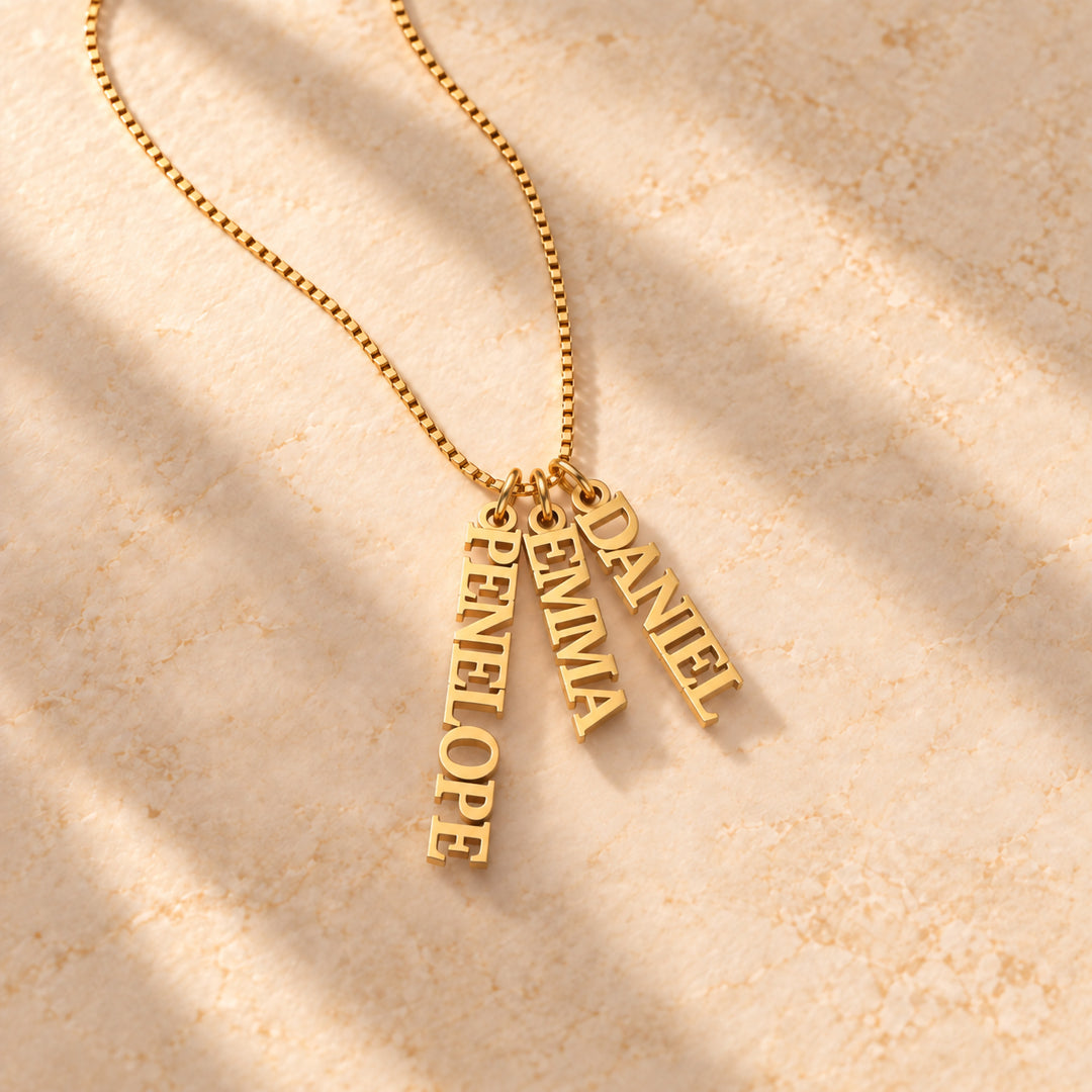 Gold vertical name plate necklace with three names in block capitals, flat lay