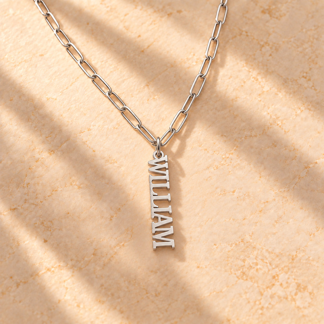 Silver vertical name plate necklace with a single name in block capitals on a paperclip chain, flat lay
