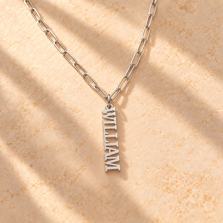 Silver vertical name plate necklace with a single name in block capitals on a paperclip chain, flat lay